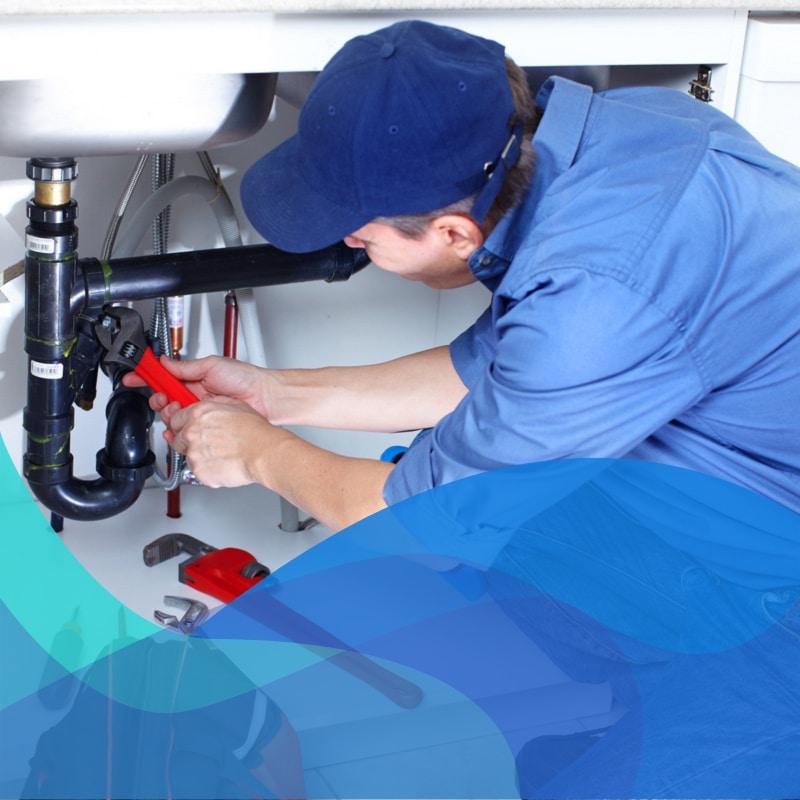 Plumber fixing sink with red wrench during 24 hour plumbing emergencies, surrounded by tools and pipes under kitchen basin.